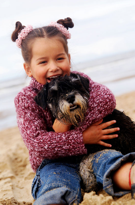 girl child with dog in arms on beach